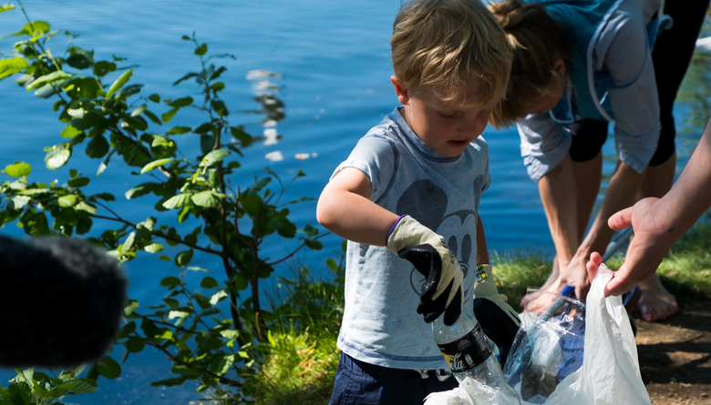 Barn som plockar skräp vid en sjö. 